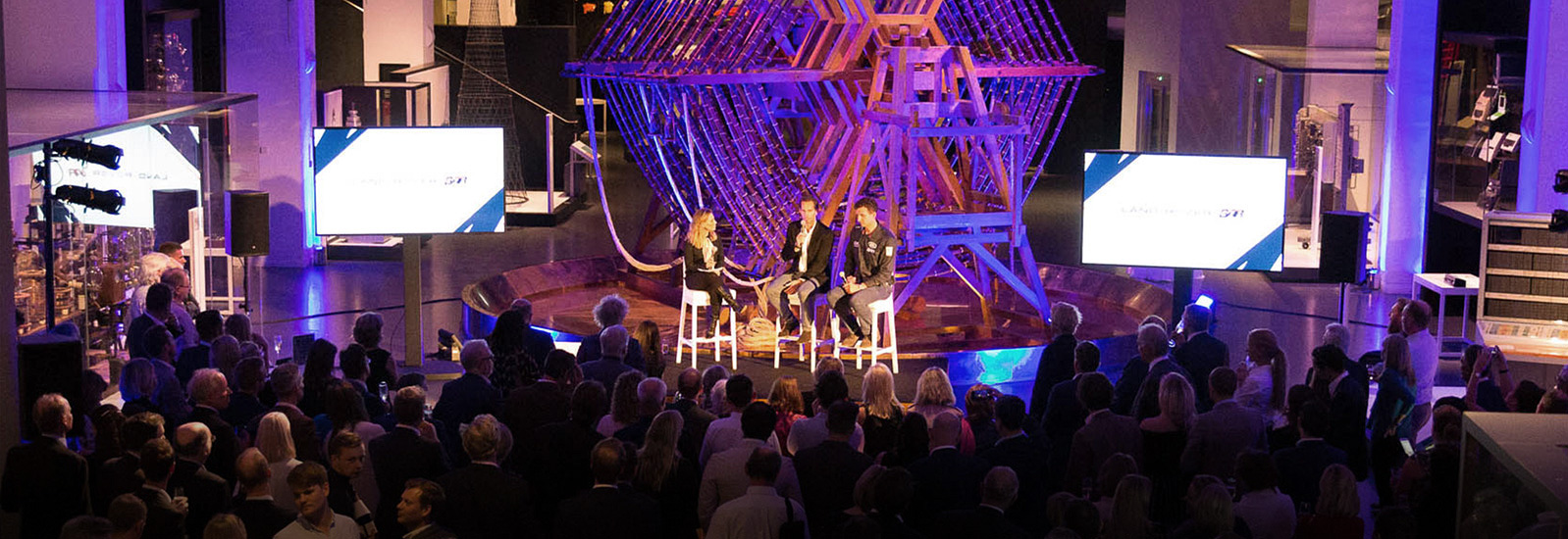 Land Rover BAR event, three guests on stage in front of the aerial tuning inductor in the Information Age gallery