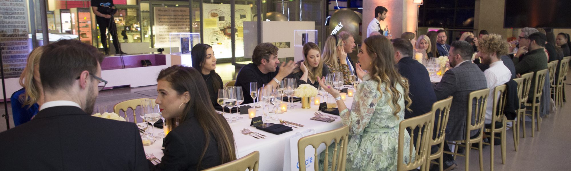 People conversing around dining table, with wine.