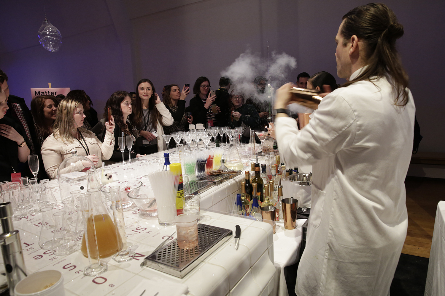 A bartender creating a cocktail with dry ice at our chemistry bar with a group of on lookers.